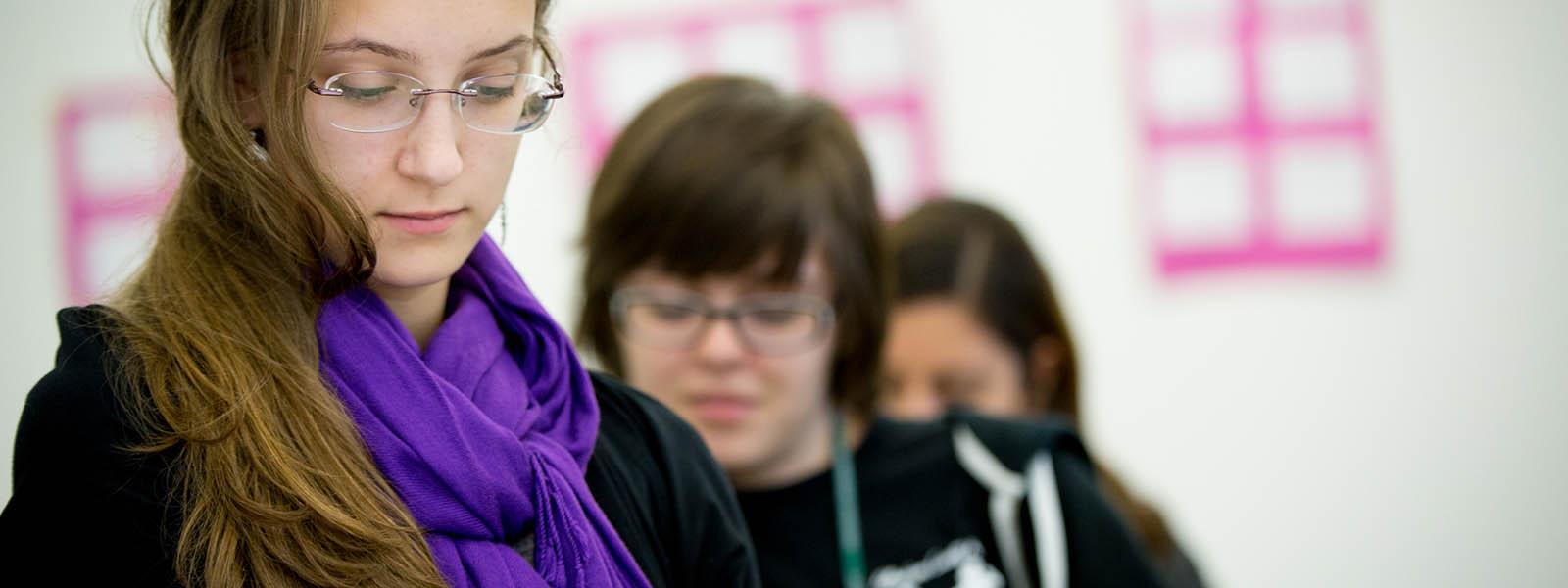 Close-up photo of a Chatham University student wearing glasses and a purple scarf, looking down