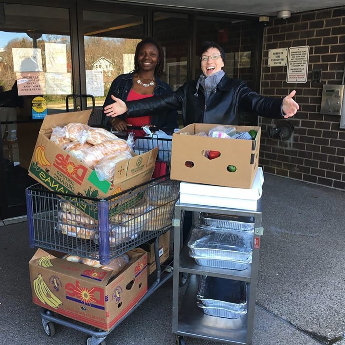 Photo of two people posing with a cartful of food outside of a grocery store entrance