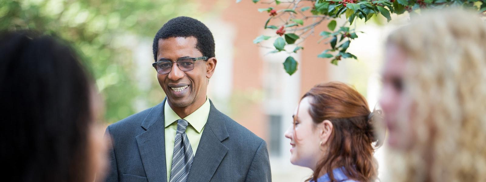 Photo of a professor wearing a suit speaking with Chatham University students outside. 