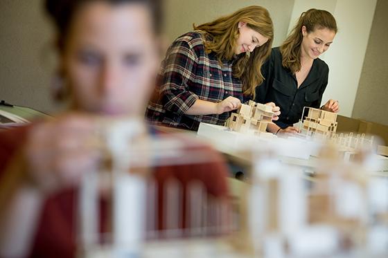 Photo of two Chatham University students working in an architecture lab building models with wood.