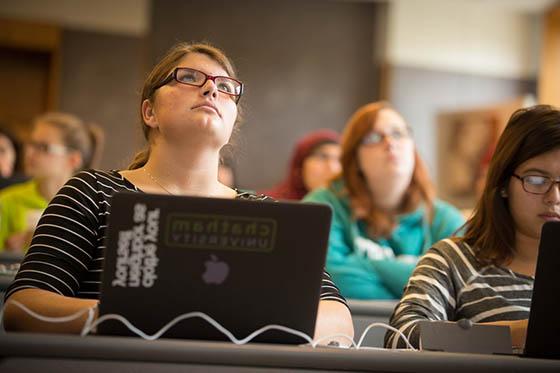 Photo of a Chatham University student paying attention in a lecture hall, with a laptop with a Chatham University sticker on it in front of her