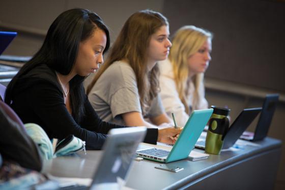 Photo of students paying attention to a lecture, with laptops and notebooks in front of them