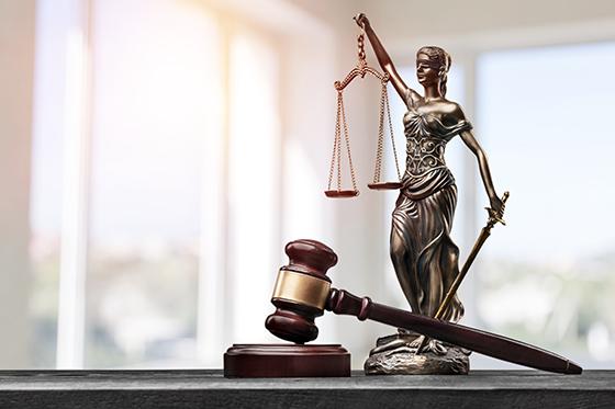 Photo of a gold statue of Justice, a blindfolded woman holding scales and a sword, with a gavel beside it